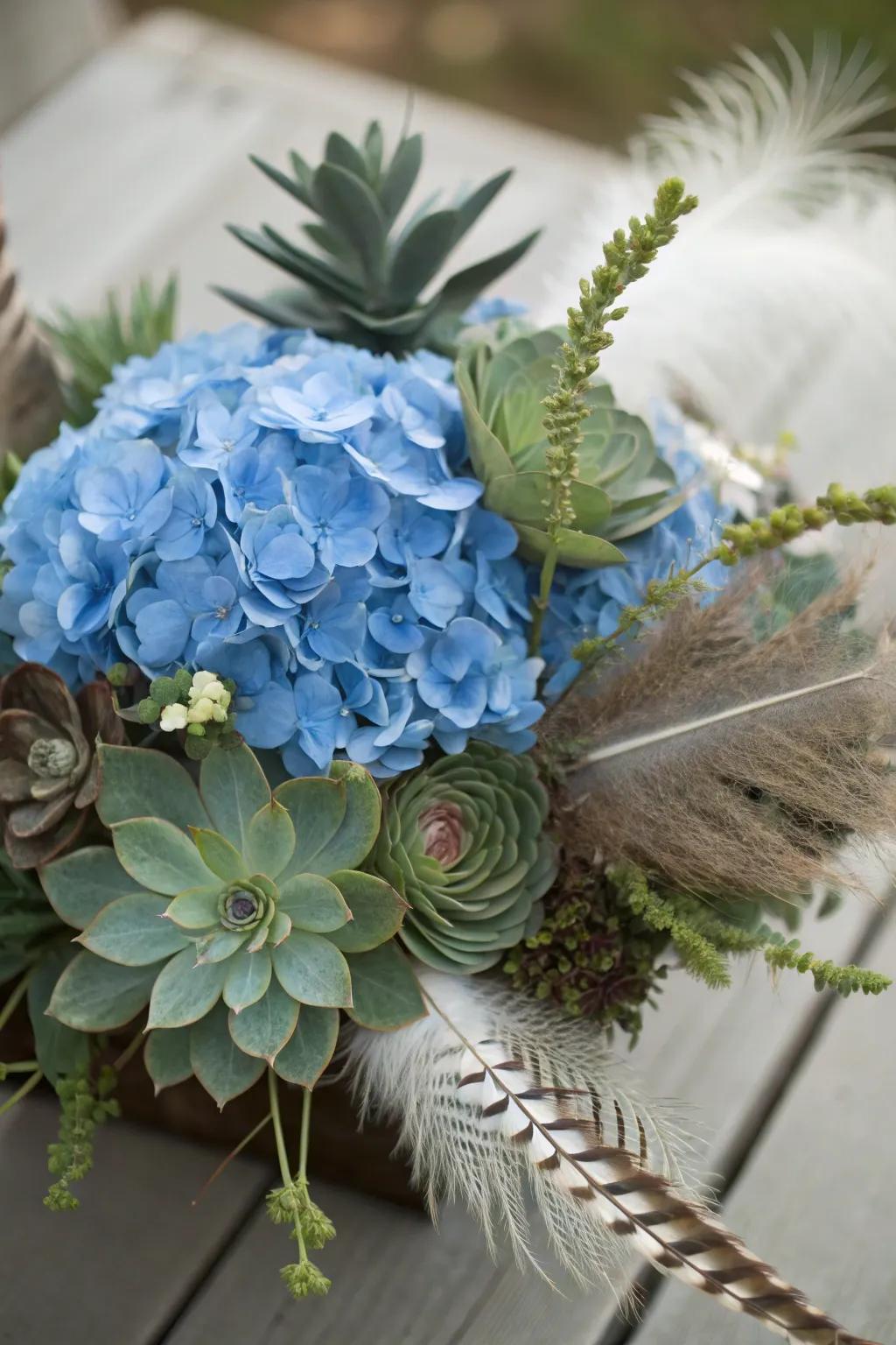 An eclectic centerpiece consisting of blue hydrangeas, succulents, and feathers.