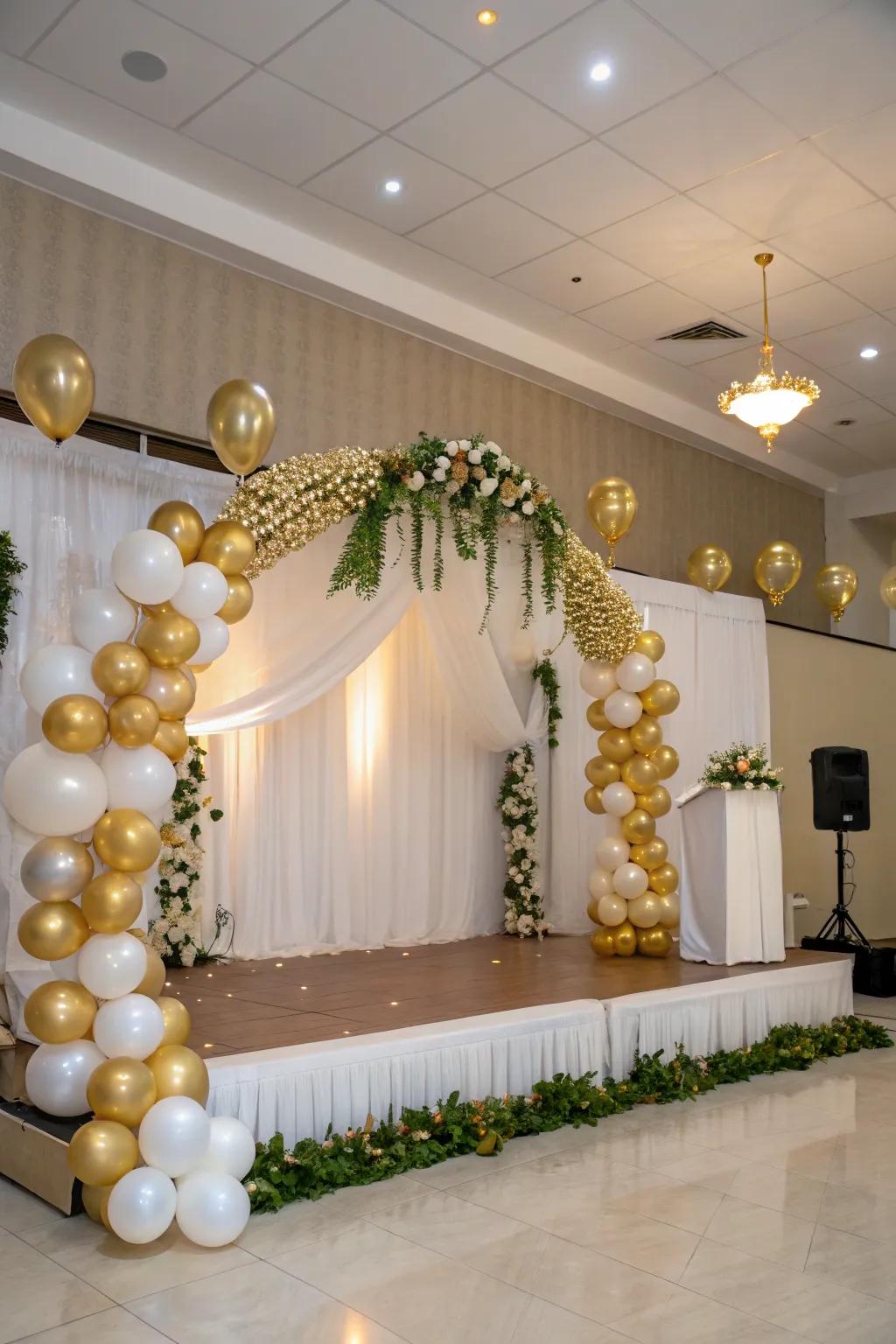 An elegant balloon arch and garland, adorned in gold and white, beautifully frames the stage.