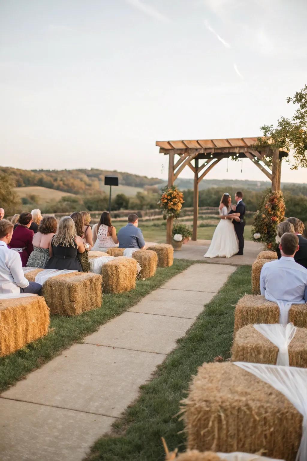 A countryside wedding ceremony with hay bale bench seating covered in comfortable material.
